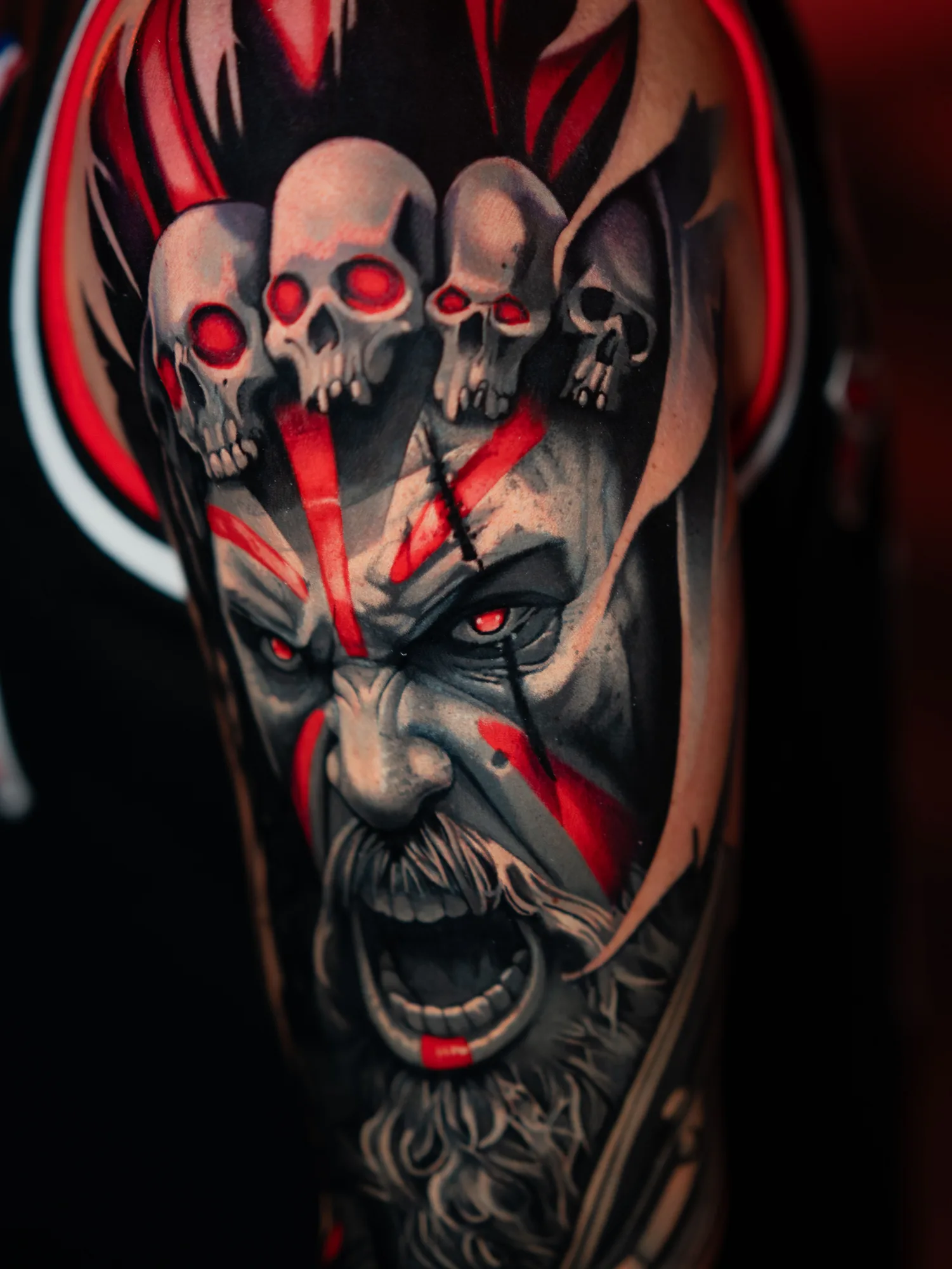 Realism tattoo of a screaming Viking under four skulls with red war paint on a shoulder
