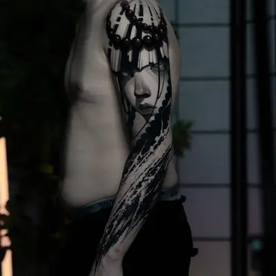 Black and grey realism portrait with calligraphy strokes running the length of an arm