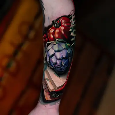 Color realism tattoo of tomatoes, a pepper and an artichoke on an inner forearm