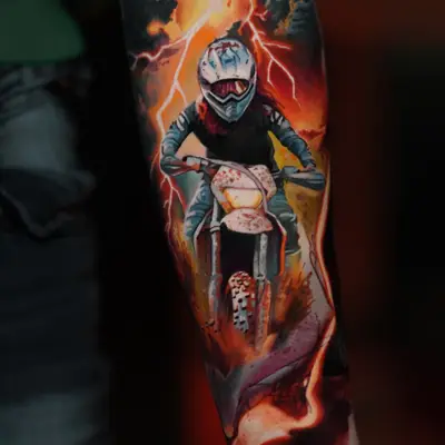 Color realism tattoo of a motocross rider coming out of fire on a forearm