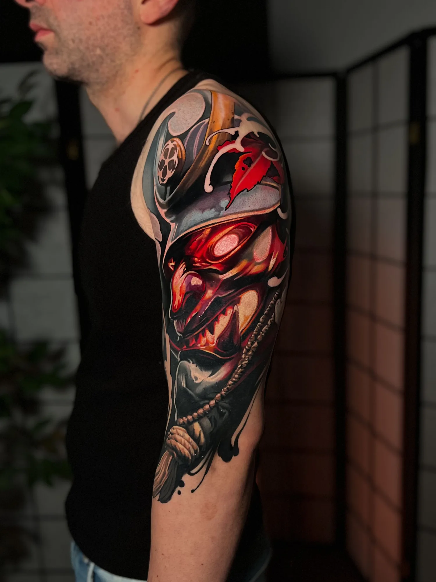 Color realism tattoo of a red Japanese demon mask on a shoulder and upper arm