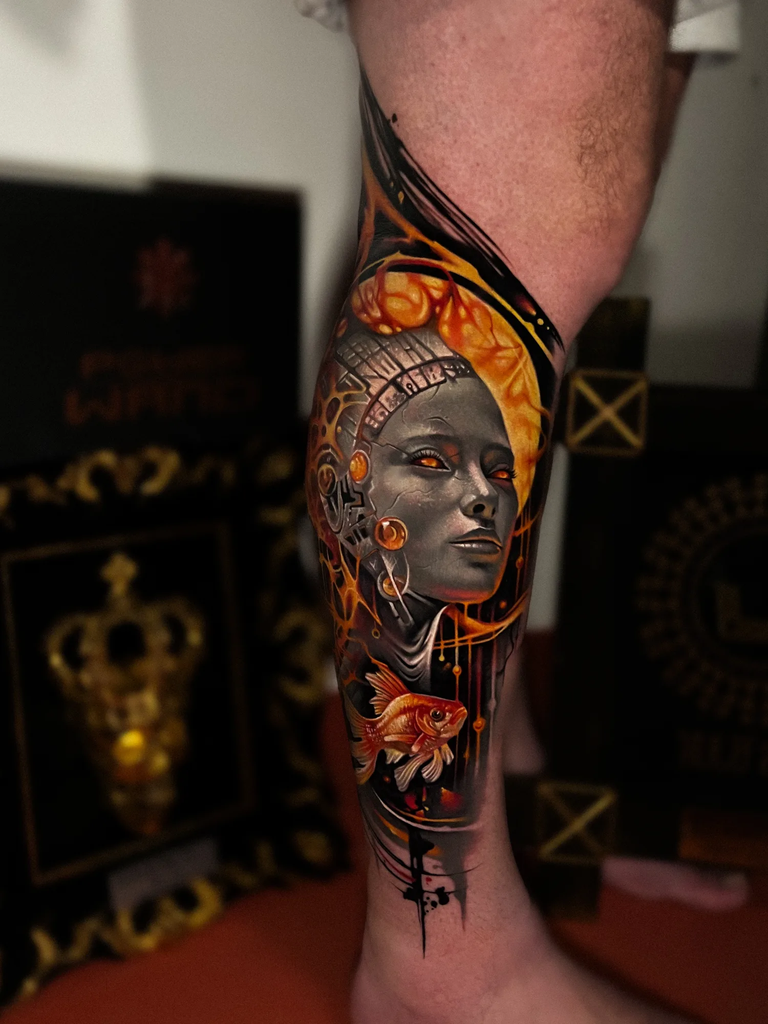 A vibrant, painterly tattoo of a woman's face and a goldfish on the leg in a surrealism style.