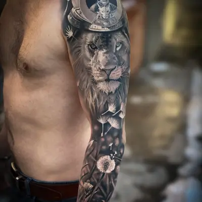 Black and grey realism full sleeve: a lion wearing a samurai kabuto helmet on the shoulder, with dandelion seeds drifting down the arm toward the wrist.