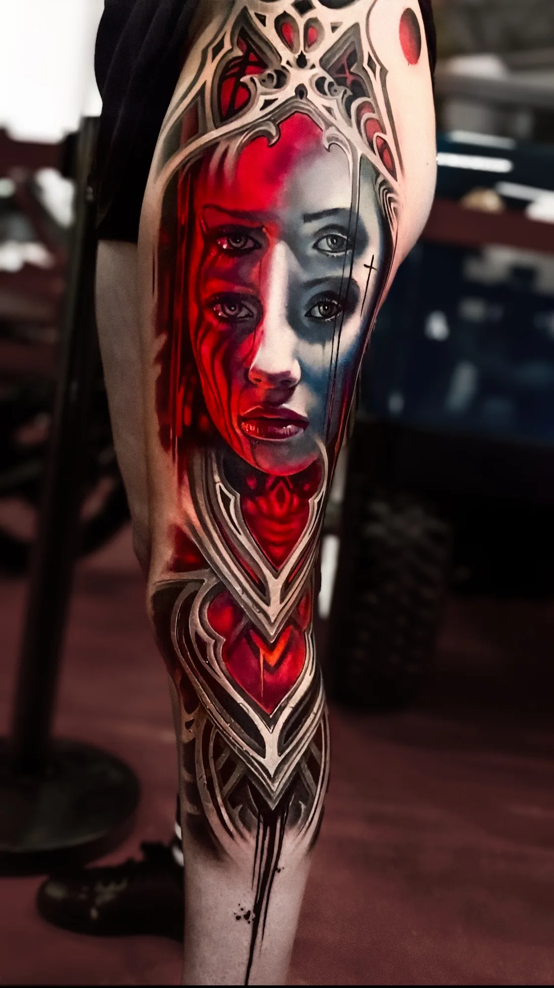 Tattoo of surreal face with multiple eyes and red accents on leg.