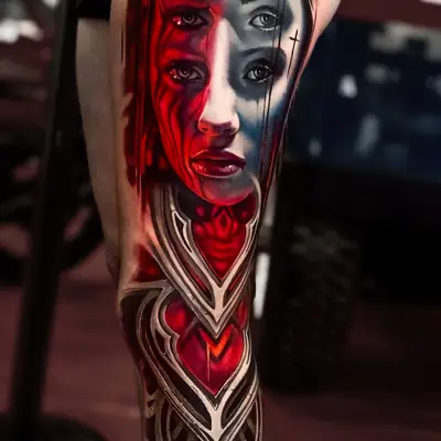 Tattoo of surreal face with multiple eyes and red accents on leg.