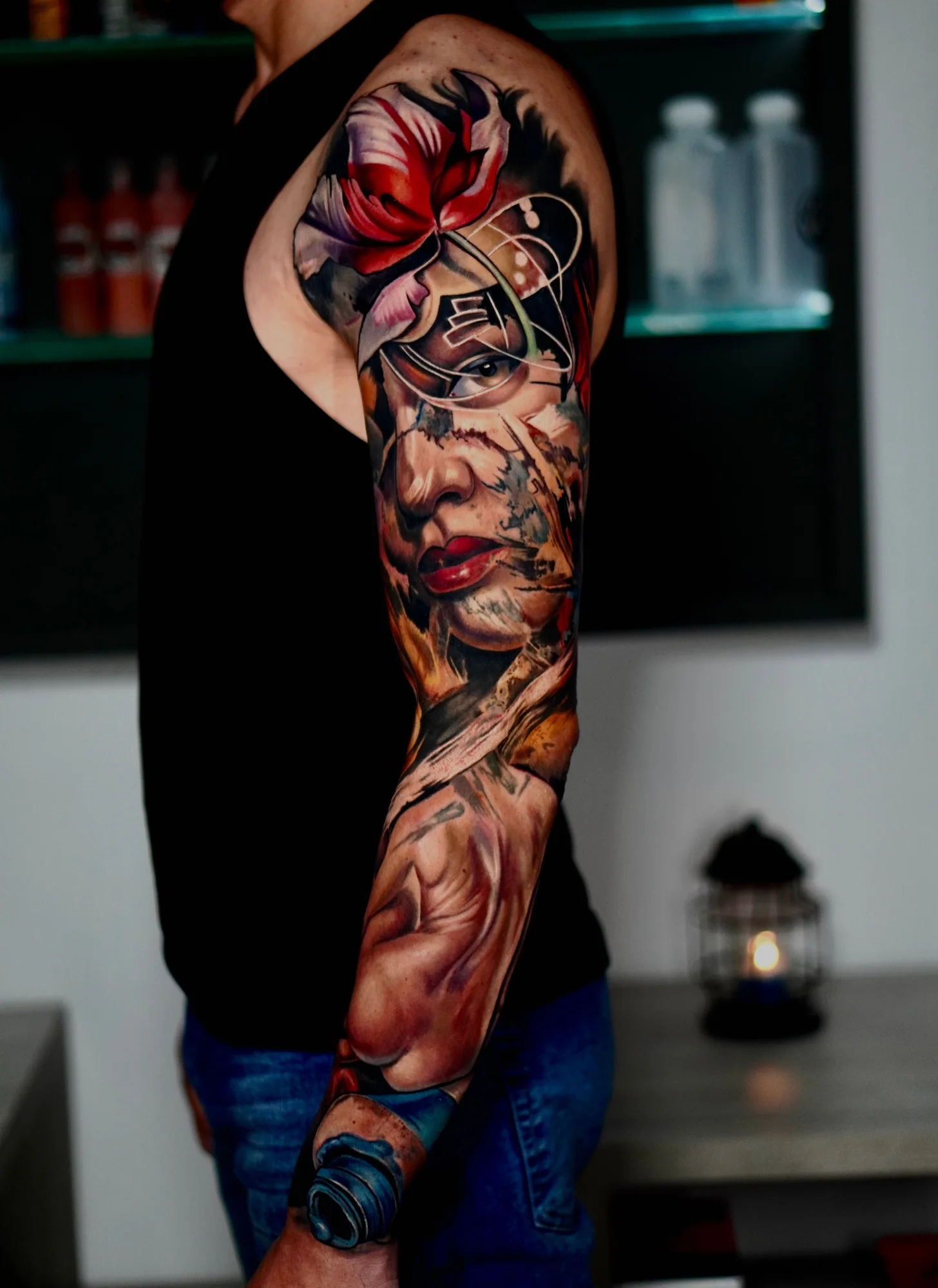 Color realism full sleeve with a red bloom at the shoulder, a woman's face and a portrait lower on the arm