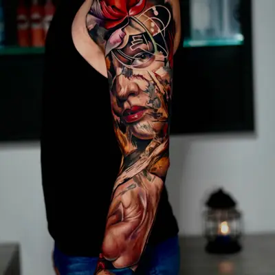 Color realism full sleeve with a red bloom at the shoulder, a woman's face and a portrait lower on the arm