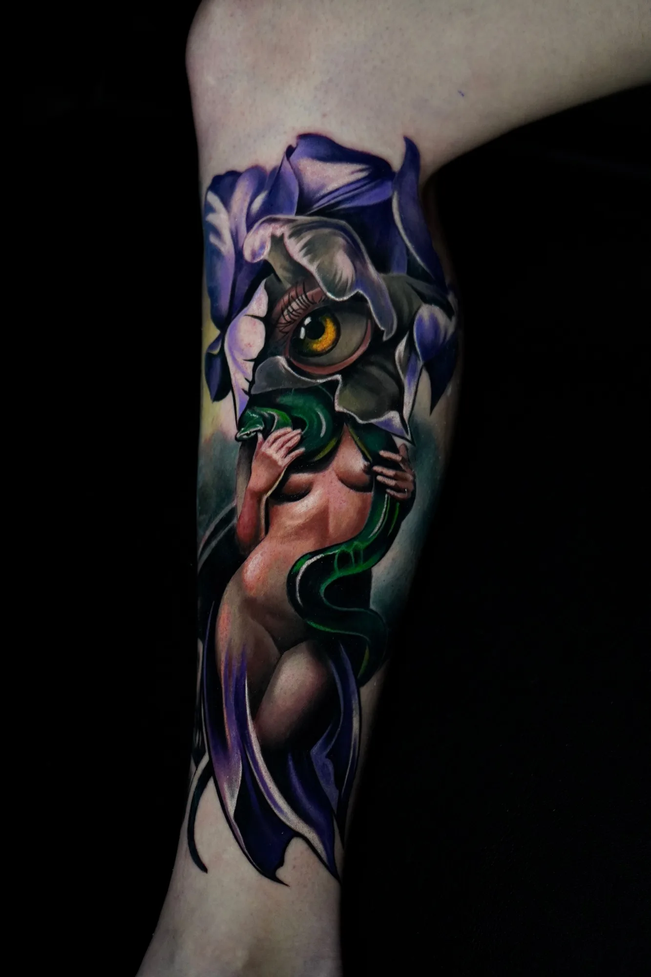 Color realism tattoo on the calf of purple irises with a figure, a green serpent and a large eye