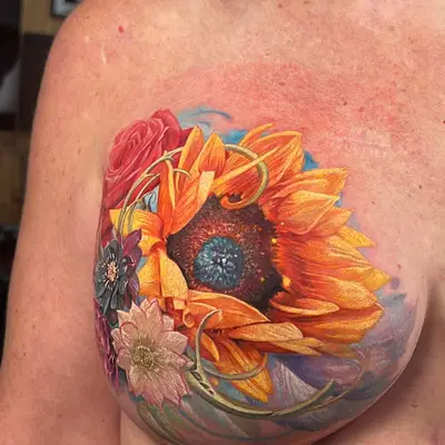A vibrant floral mastectomy scar coverup tattoo featuring sunflowers and roses on a woman's chest.