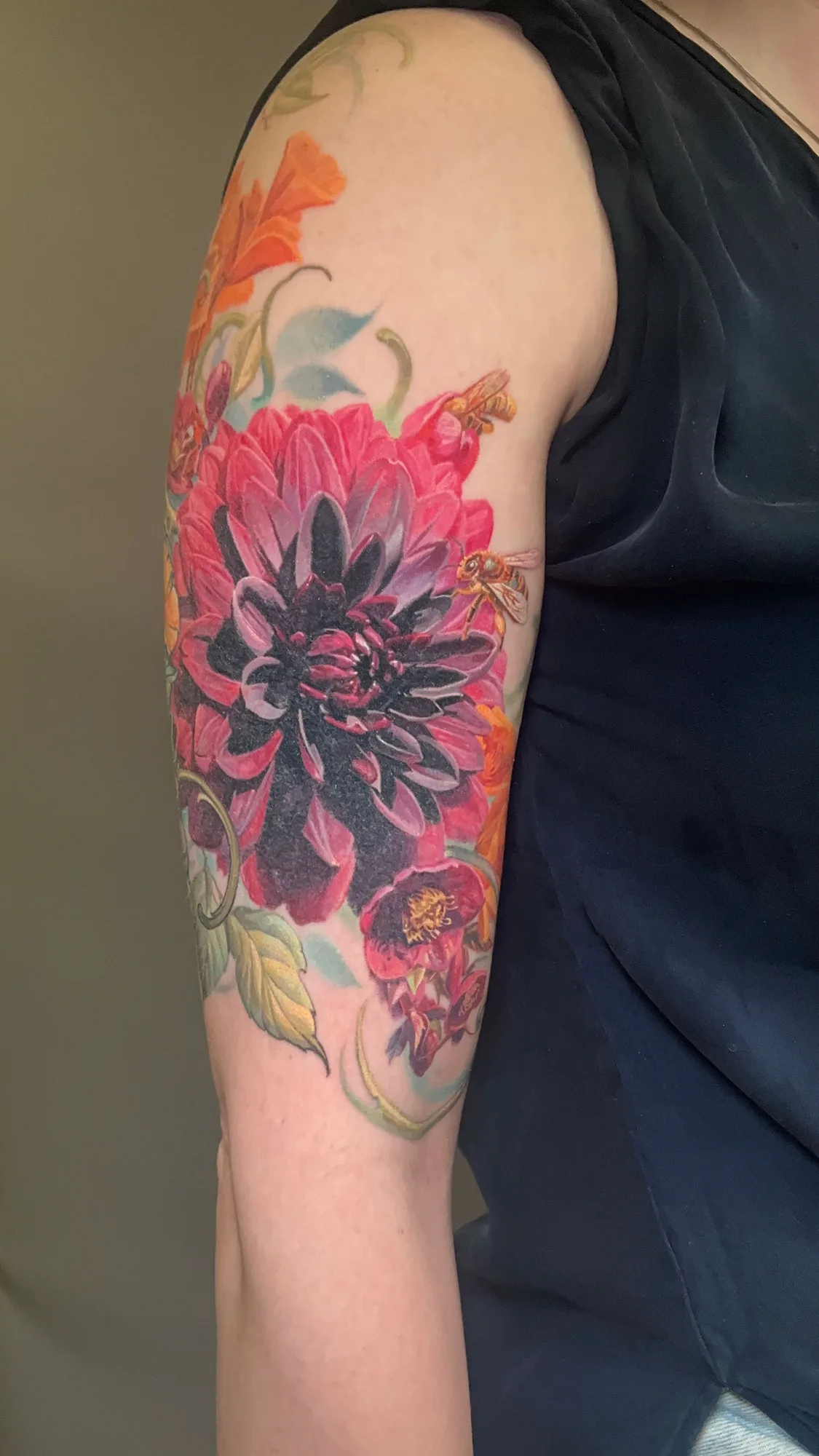 A vibrant floral tattoo featuring large peonies, dahlias, and poppies and bees on the arm.