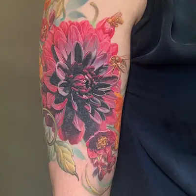 A vibrant floral tattoo featuring large peonies, dahlias, and poppies and bees on the arm.