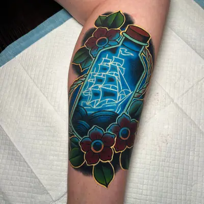 Colorful tattoo of a ship in a bottle in a neon style surrounded by flowers on a calf.