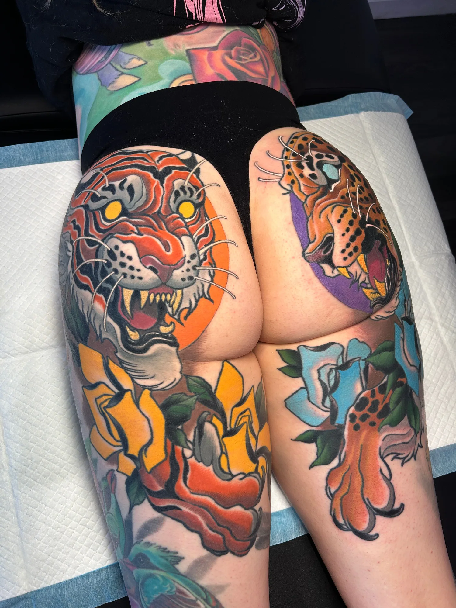 Neotraditional tattoos of complementary tiger and jaguar on a person's but.