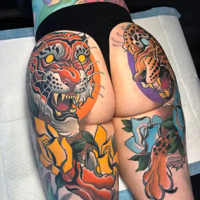 Neotraditional tattoos of complementary tiger and jaguar on a person's but.