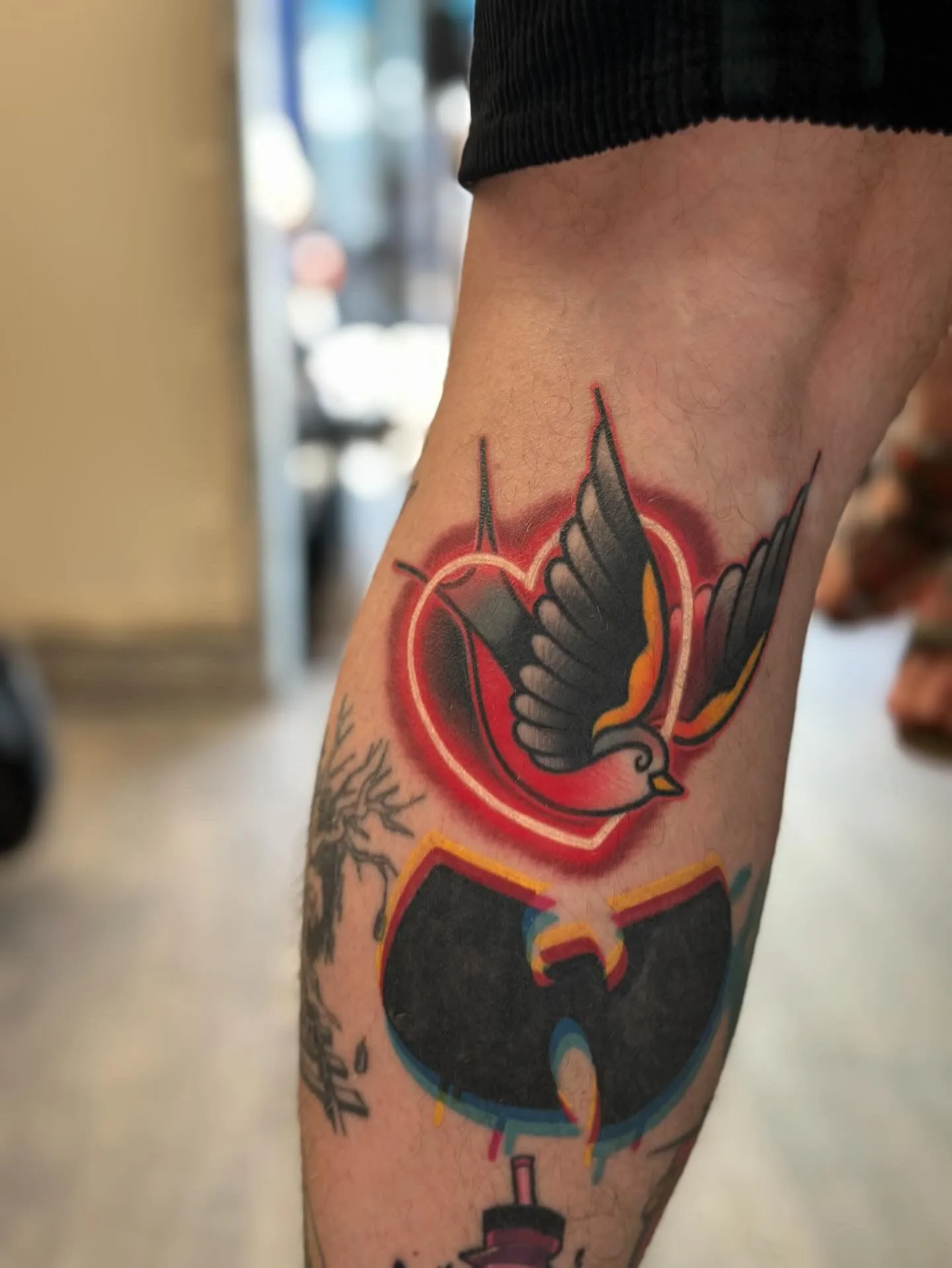 Tattoo of an American traditional swallow encircled with a neon heart.