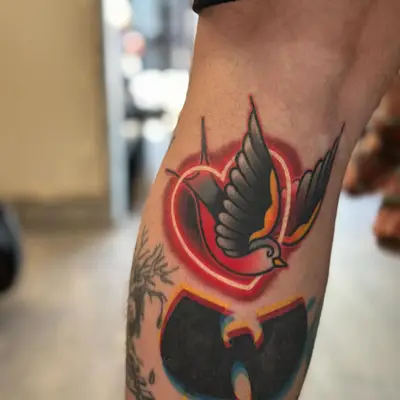Tattoo of an American traditional swallow encircled with a neon heart.
