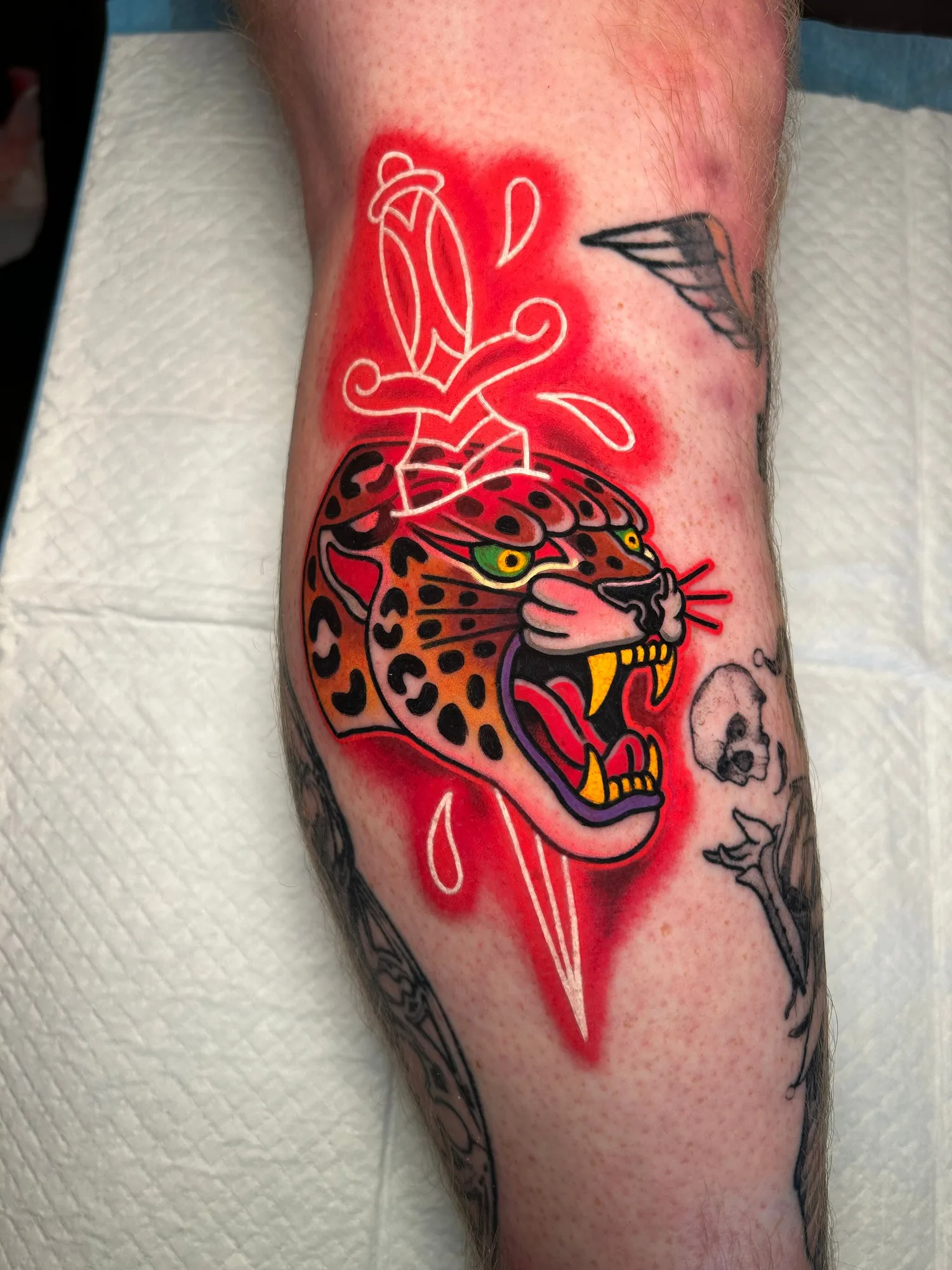 A jaguar head with a neon dagger and red background on a forearm tattoo.