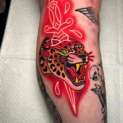 A jaguar head with a neon dagger and red background on a forearm tattoo.