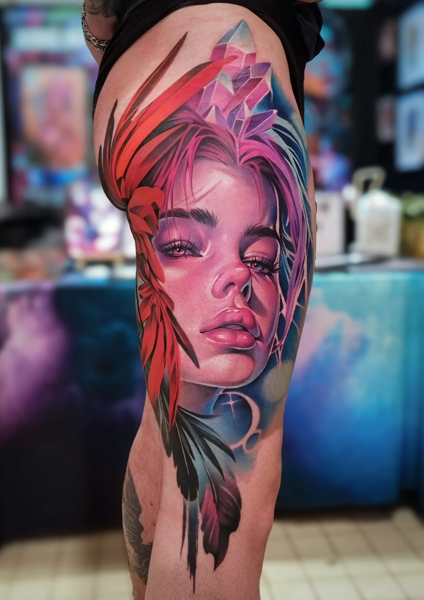 Realistic tattoo of a woman's face with colorful crystal and feather elements.