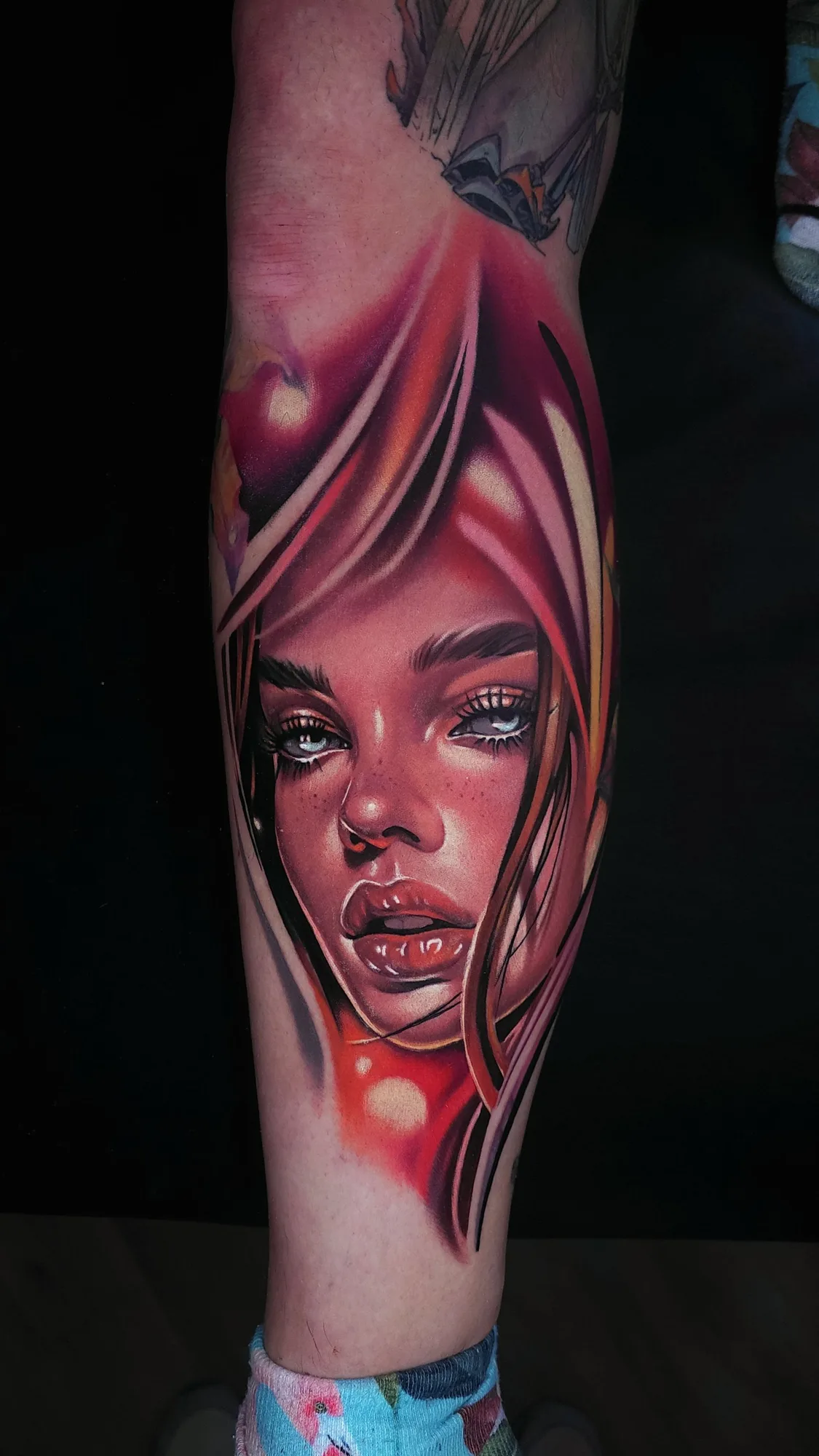 Color neorealist portrait of a woman framed by flowing red and pink hair with pale blue eyes and freckles, tattooed on the calf.